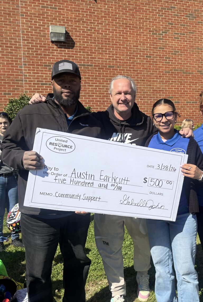 United Resource Project presents a $500 check to Austin Earlycutt during a community outreach event surrounded by supporters.