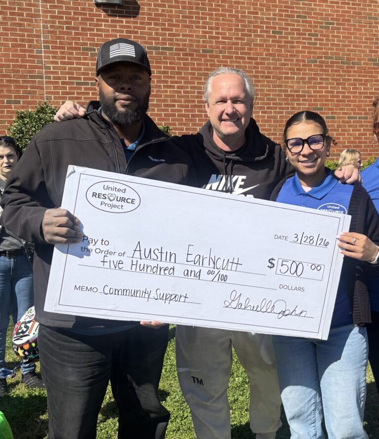 United Resource Project presents a $500 check to Austin Earlycutt during a community outreach event surrounded by supporters.